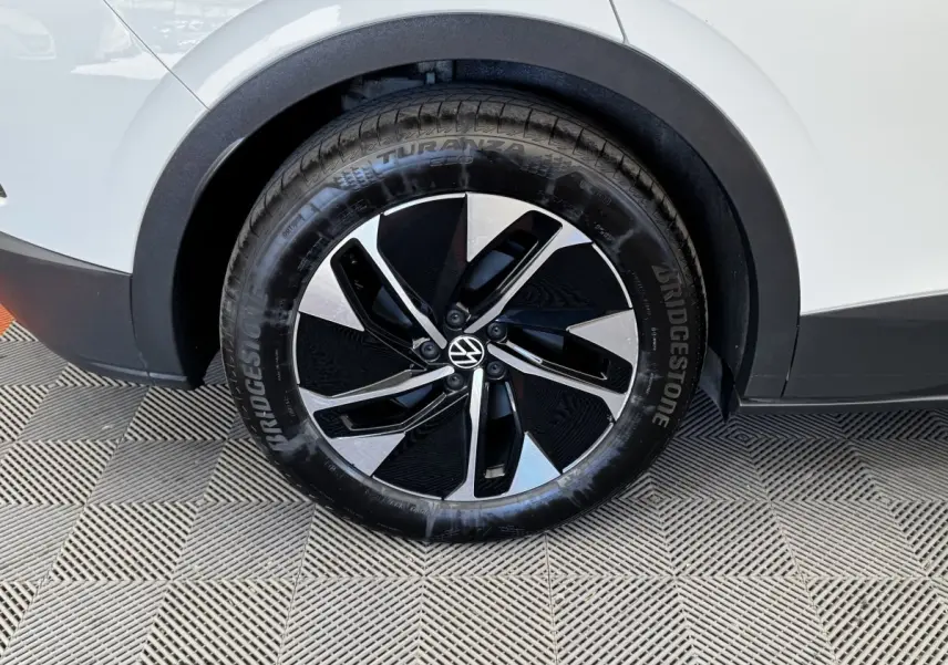 Gros plan sur la roue avant droite du Volkswagen ID.4 blanc, avec jante noire et argentée au design moderne.