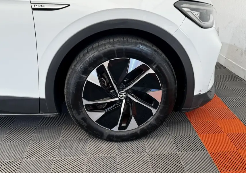 Gros plan sur la roue avant droite d’un Volkswagen ID.4 blanc avec jante noire et argentée, badge Pro visible.