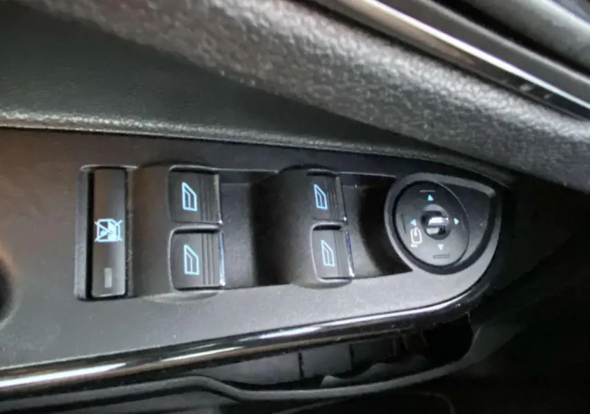 Gros plan sur les commandes de lève-vitres et réglage des rétroviseurs côté conducteur d'une Ford B-MAX blanche.