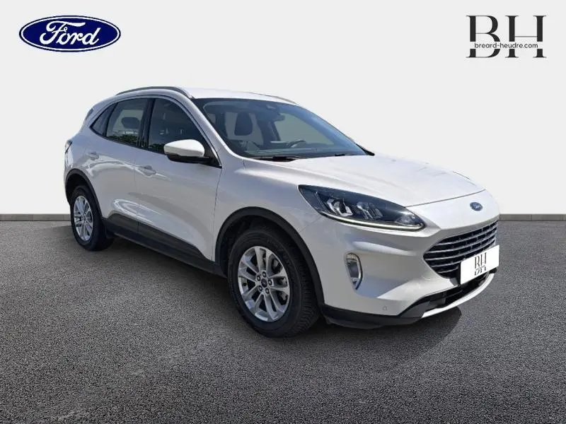 Ford Kuga blanc glacier en vue 3/4 avant droit, avec jantes alu et barres de toit visibles.