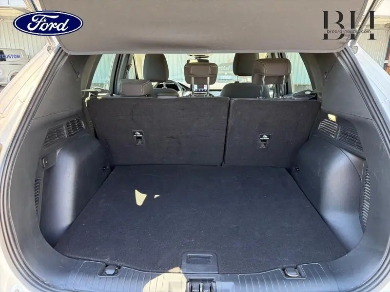 Vue intérieure du coffre spacieux du Ford Kuga blanc glacier, avec banquette arrière noire rabattue partiellement.