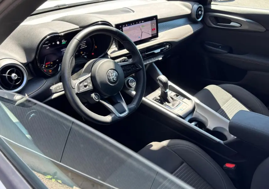 Vue intérieure côté conducteur de l'Alfa Romeo Tonale 2025, volant cuir, écran tactile et console centrale avec levier de vitesses.