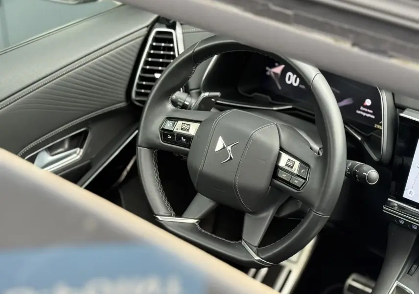 Vue rapprochée du volant en cuir noir du DS7 2025, avec tableau de bord numérique et détails de la porte côté gauche.