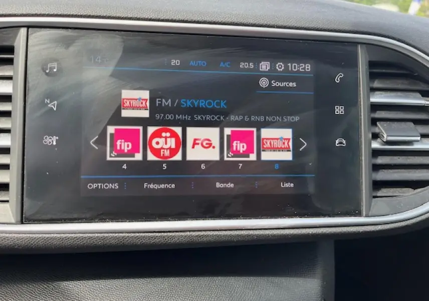 Écran tactile central de la Peugeot 308 gris clair affichant la radio FM sur Skyrock, avec commandes climatisation visibles.