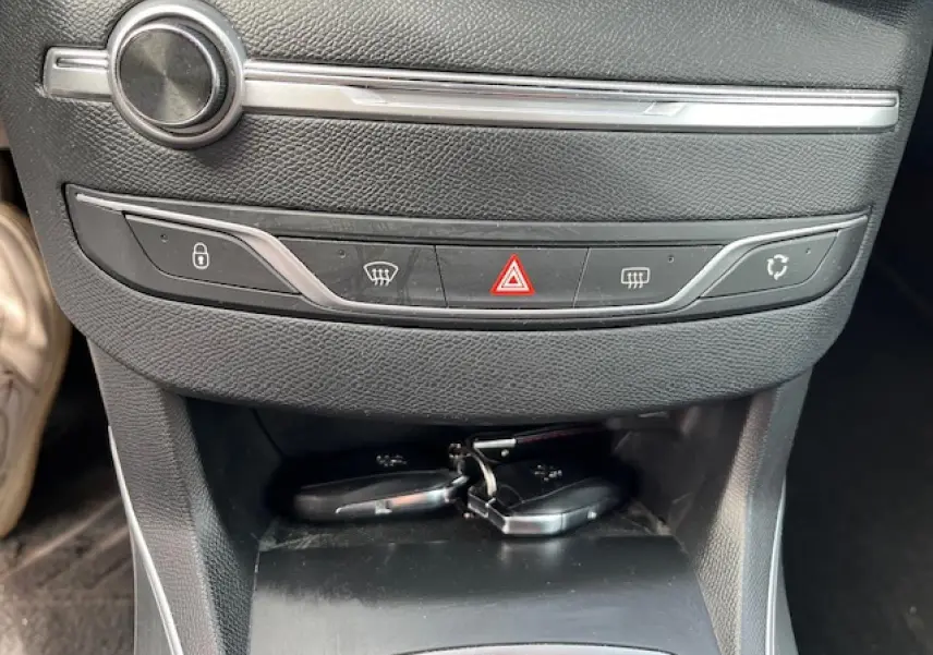 Gros plan sur la console centrale noire de la Peugeot 308 avec les boutons de verrouillage, désembuage et feux de détresse, clés posées dessous.