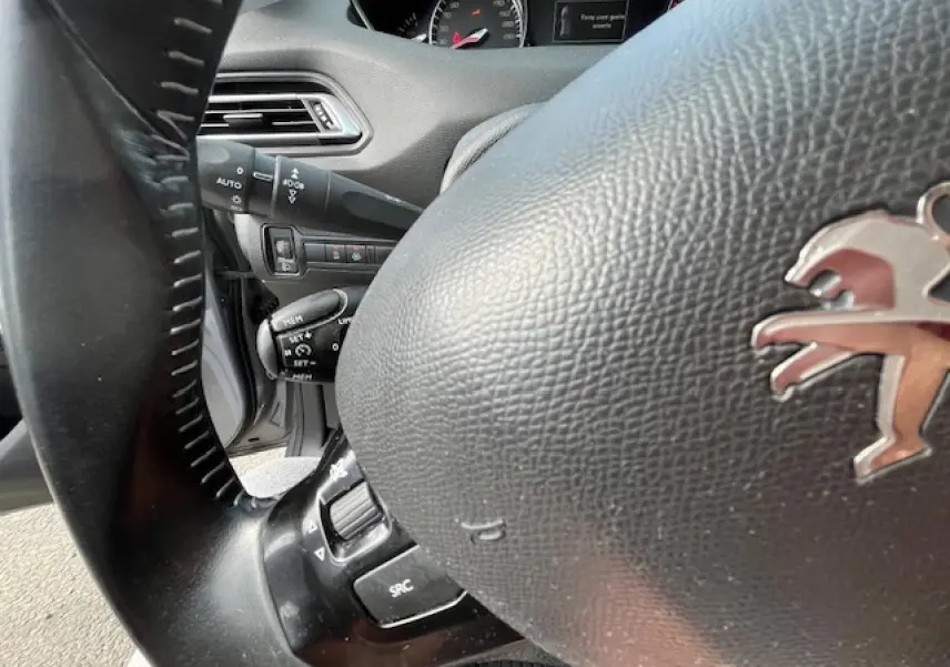 Gros plan sur le volant noir de la Peugeot 308 2018, avec commandes intégrées et tableau de bord partiellement visible.