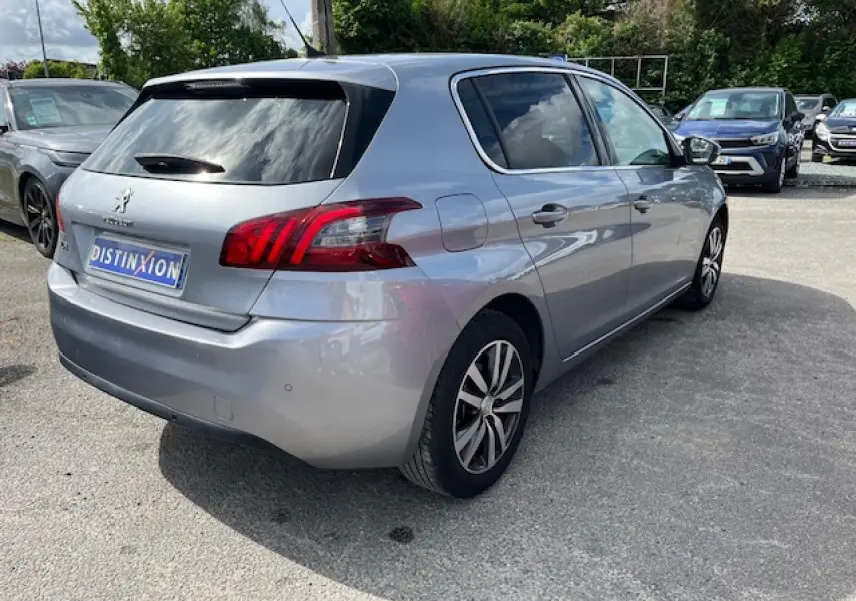 Peugeot 308 gris clair vue 3/4 arrière droit, avec feux arrière distinctifs et jantes alliage bicolores.