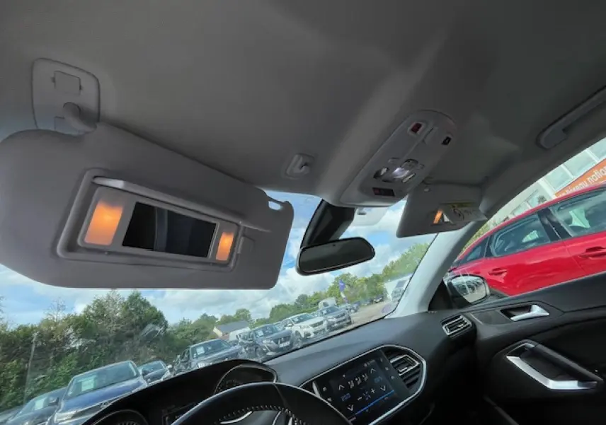 Vue intérieure avant de la Peugeot 308 gris clair, avec pare-soleil allumé et tableau de bord moderne visible.