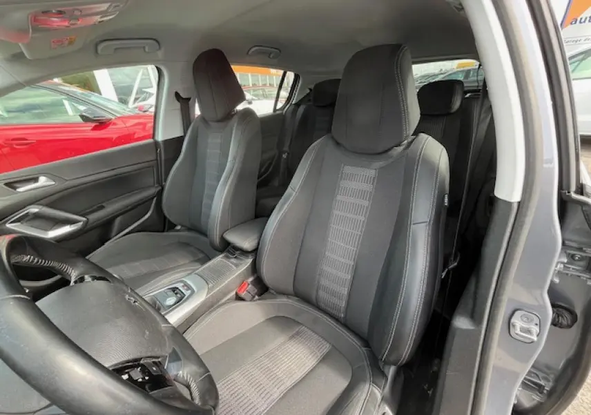 Vue intérieure côté droit montrant les sièges avant noirs et gris d'une Peugeot 308 gris clair de 2018 avec accoudoir central.