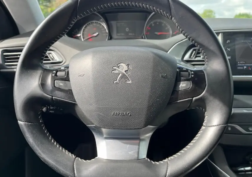 Vue rapprochée du volant noir de la Peugeot 308 gris clair, avec tableau de bord et écran tactile en arrière-plan.