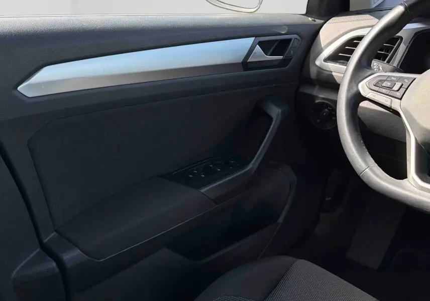 Vue intérieure côté conducteur du Volkswagen T-Roc 2025, montrant la porte noire avec commandes des vitres et volant cuir multifonctions.