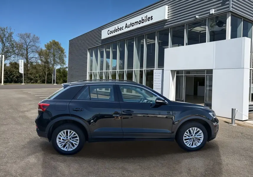 Profil côté gauche du Volkswagen T-Roc noir 2025, avec jantes alliage 16'' et rétroviseurs électriques devant un concessionnaire.