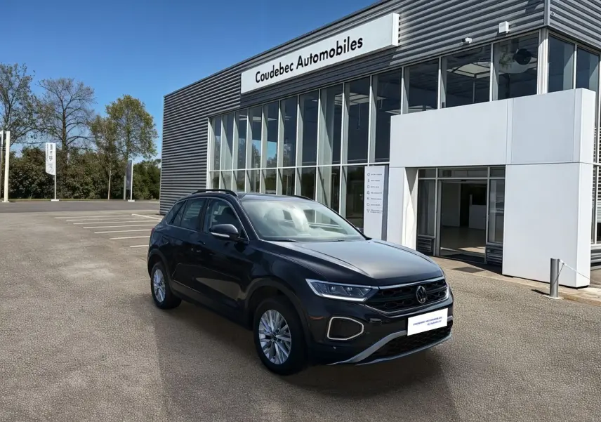 Volkswagen T-Roc noir vue 3/4 avant droit devant un bâtiment moderne de concession automobile.