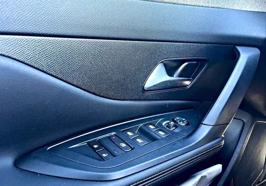 Gros plan sur la porte côté gauche intérieure noire de la Peugeot 308 1.5 BlueHDi 130 avec commandes des vitres et poignée.