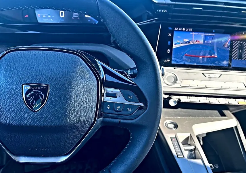 Vue rapprochée du volant multifonction noir et du tableau de bord digital avec écran tactile affichant la caméra de recul d’une Peugeot 308.