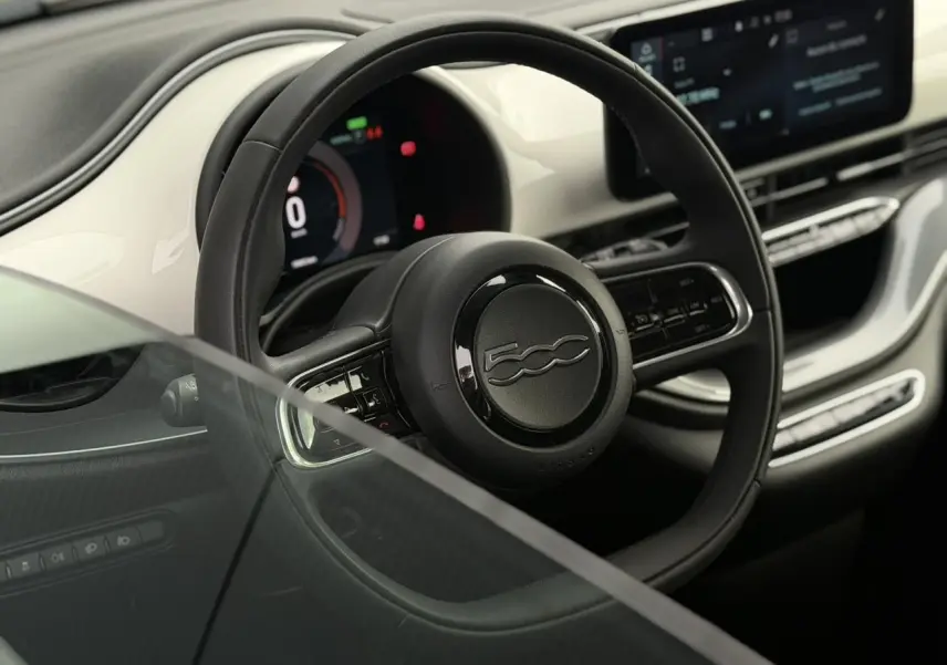 Vue intérieure rapprochée du volant noir et du tableau de bord blanc brillant de la Fiat 500 électrique 2024.