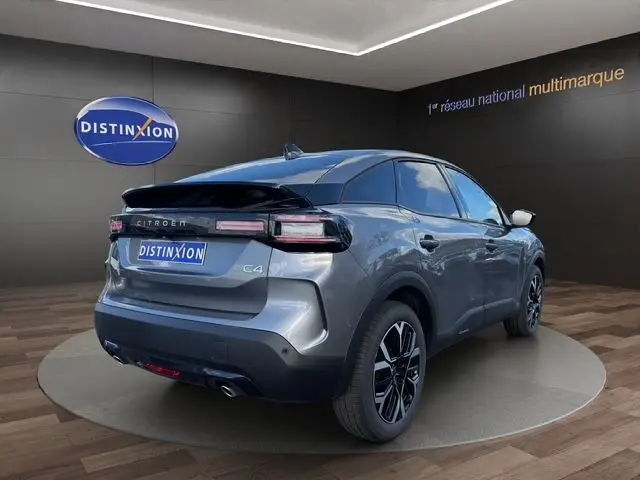 Vue 3/4 arrière droite d'une Citroën C4 Hybrid 145 gris Mercury avec jantes alliage et toit noir en showroom.
