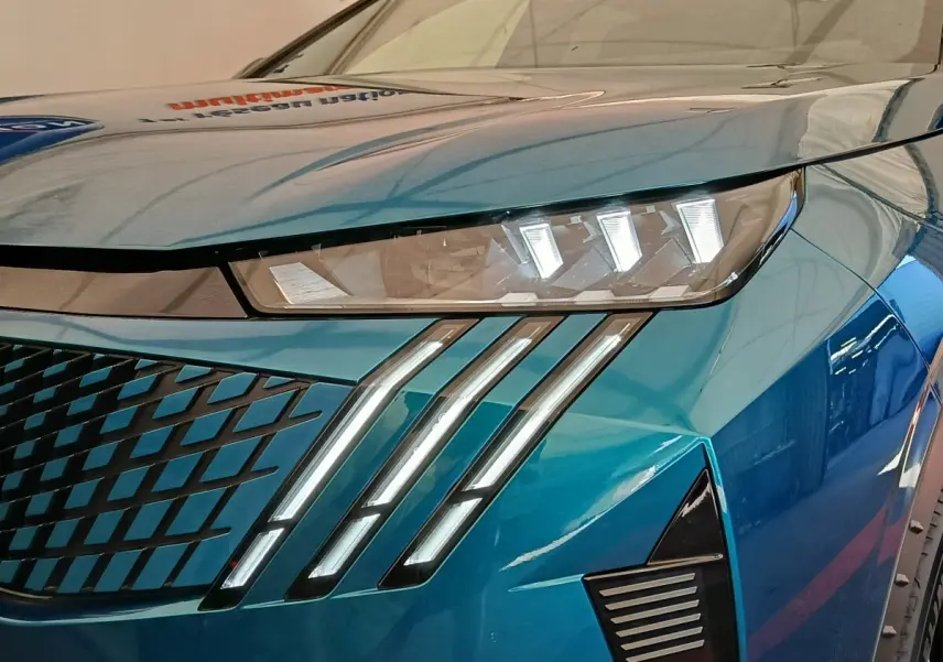 Gros plan sur le phare avant droit et la calandre bleue du Peugeot 3008 1.2 Hybrid 136 GT 2025.