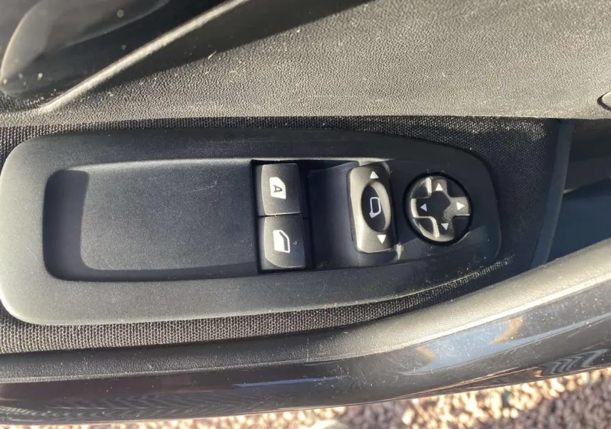 Gros plan sur les commandes de réglage des rétroviseurs et des vitres côté conducteur d’une Peugeot 208 noire de 2016.