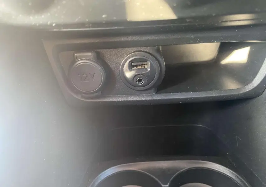 Prise 12V et port USB avec prise jack dans l'habitacle d'une Peugeot 208 noire, vue rapprochée du compartiment central.