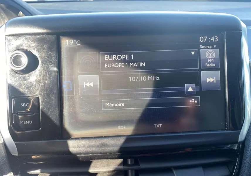 Écran tactile central de la Peugeot 208 noir, affichant la radio Europe 1 à 07:43, avec commandes autour.