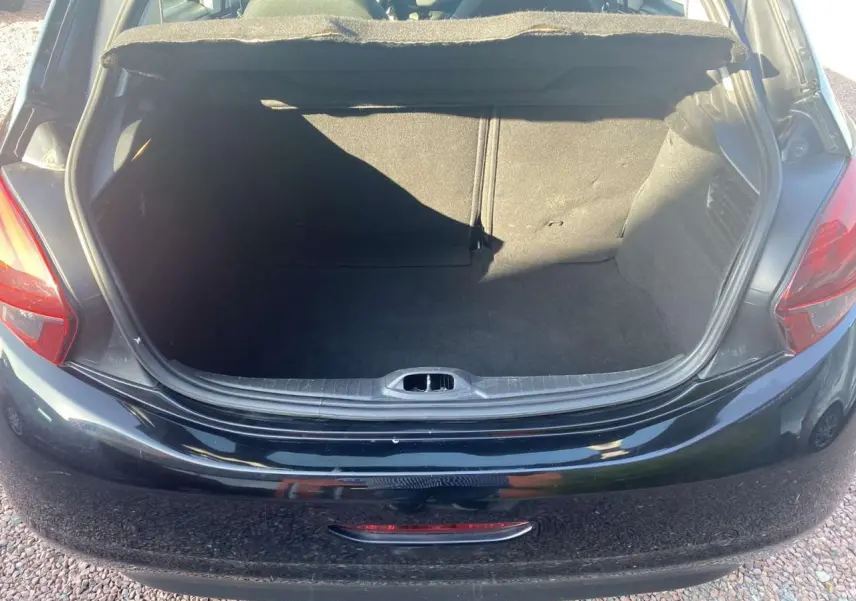 Coffre ouvert vu de l'arrière d'une Peugeot 208 noire, montrant l'espace de chargement vide et la peinture métallisée.
