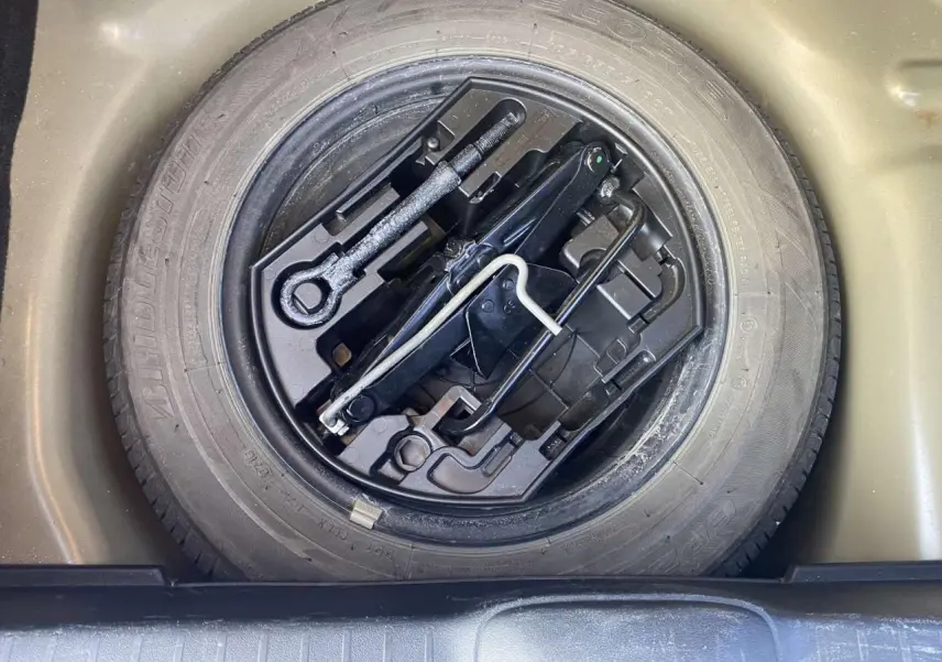 Gros plan sur la roue de secours acier 15 pouces et les outils de bord du coffre d'une Peugeot 208 noire.