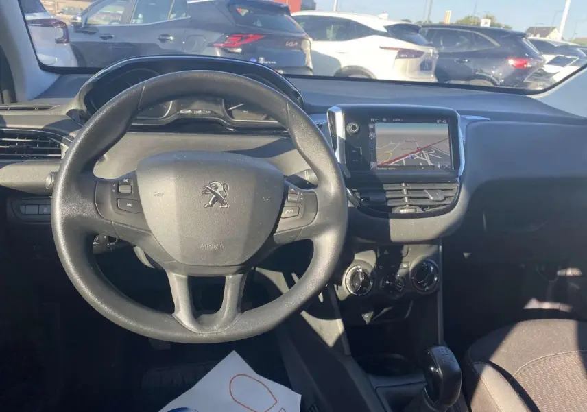 Vue intérieure centrée sur le volant Peugeot et l'écran tactile GPS, avec tableau de bord et levier de vitesse visibles.