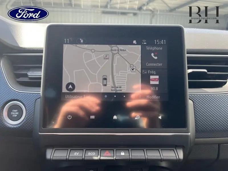 Écran tactile central du tableau de bord du Renault Arkana blanc perle, affichant la navigation et les commandes multimédia.
