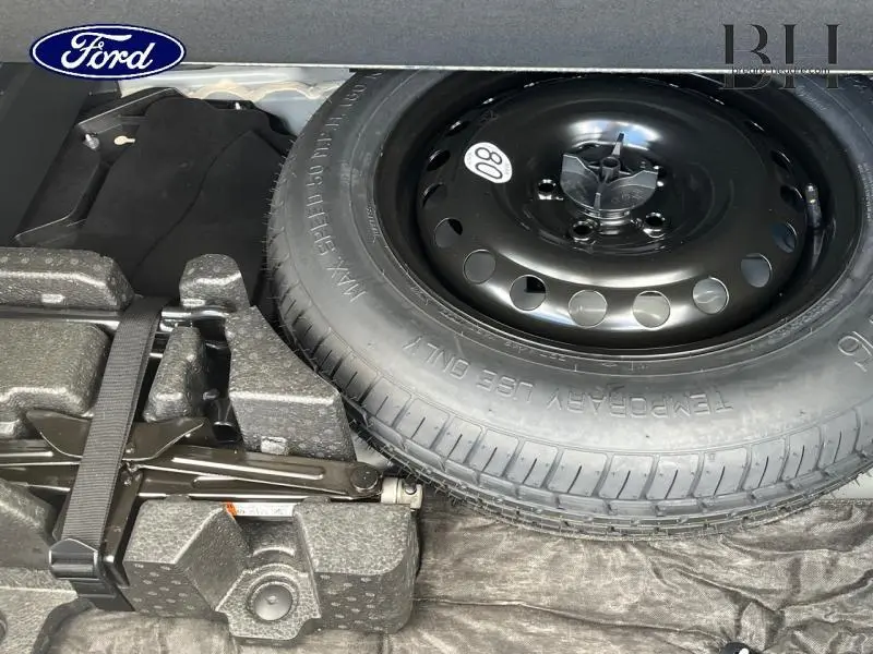 Gros plan sur la roue de secours temporaire noire et son équipement dans le coffre d'un Renault Arkana blanc perle.