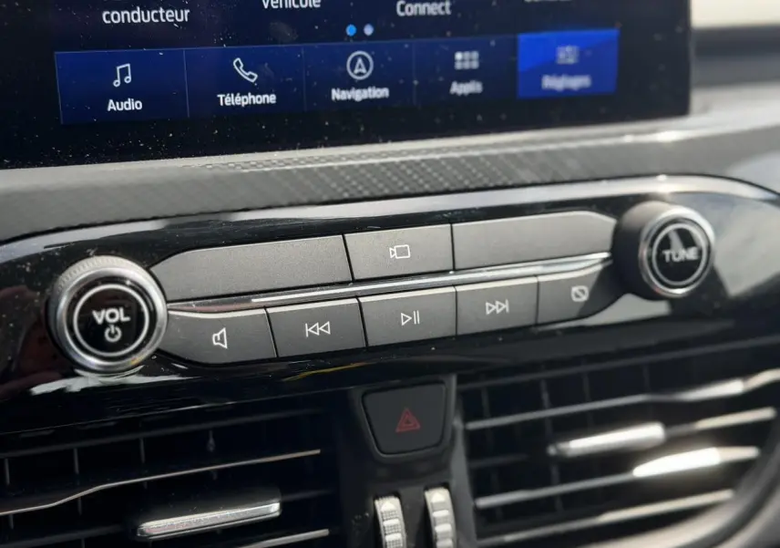 Gros plan sur la console centrale noire du Ford Kuga gris Solar 2023 avec commandes audio et écran tactile partiel visible.