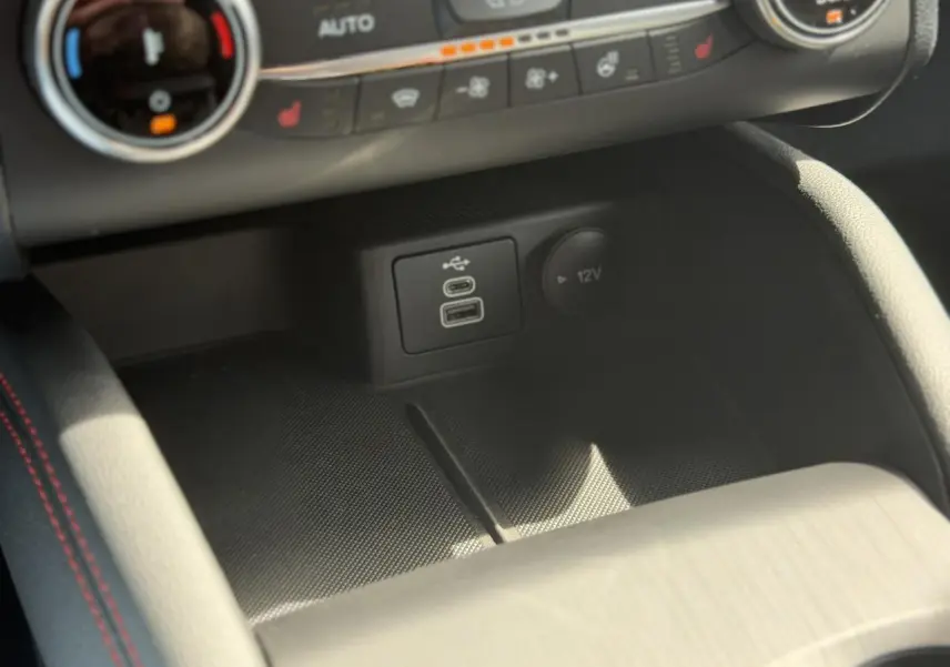 Gros plan sur la console centrale du Ford Kuga gris Solar, montrant les ports USB et la prise 12V avec surpiqûres rouges.