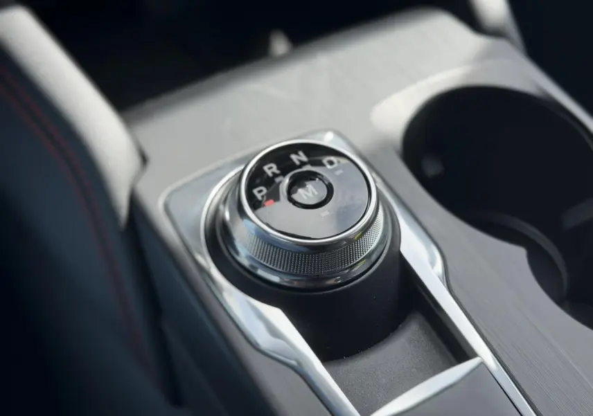 Gros plan sur le sélecteur rotatif de la boîte automatique du Ford Kuga gris Solar, avec console centrale et porte-gobelets.