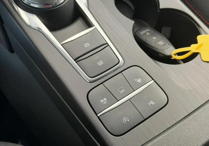 Gros plan sur la console centrale du Ford Kuga gris Solar 2023, avec boutons de contrôle et clé dans porte-gobelet.