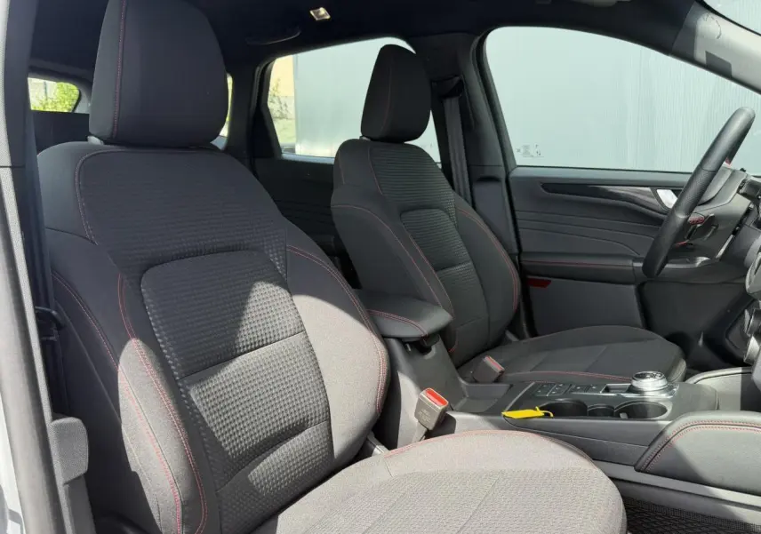 Vue intérieure côté gauche montrant les sièges avant noirs avec surpiqûres rouges du Ford Kuga ST-Line 2023.