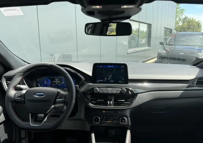 Vue intérieure avant du Ford Kuga 2023 ST-Line, tableau de bord noir avec écran tactile central et volant multifonction à surpiqûres rouges.