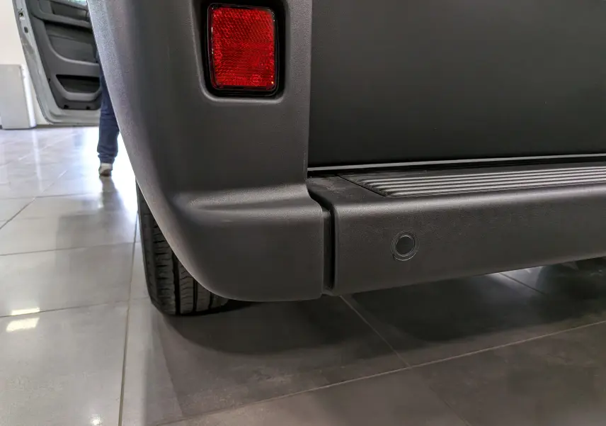 Gros plan sur le pare-chocs arrière noir du Fiat Ducato Fourgon blanc, avec feu rouge et capteur de recul visible.