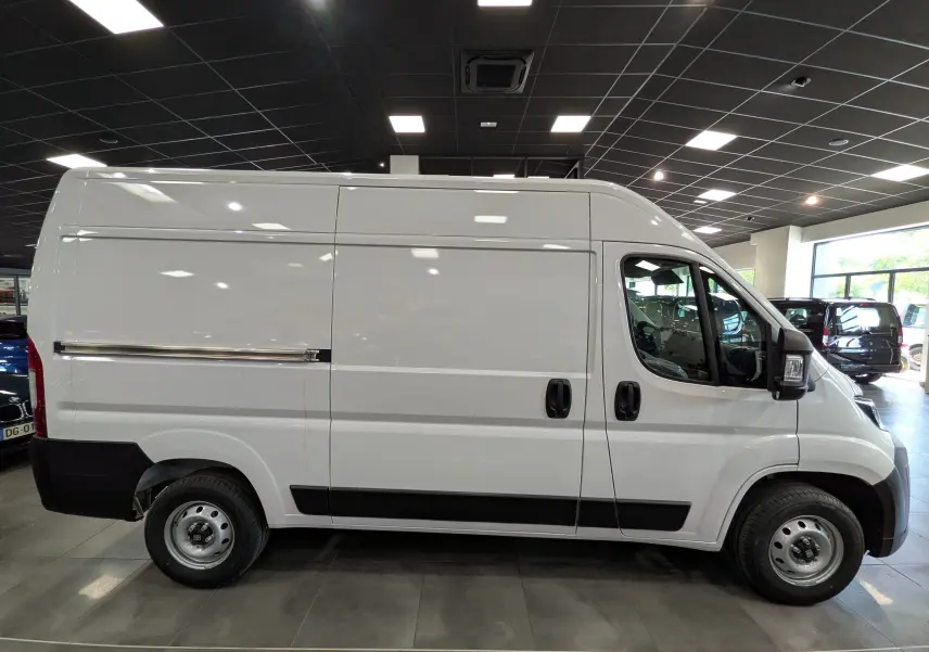 Vue de profil côté gauche d'un fourgon blanc Fiat Ducato M H2 3.3T Diesel 2026 en showroom, avec protections noires.