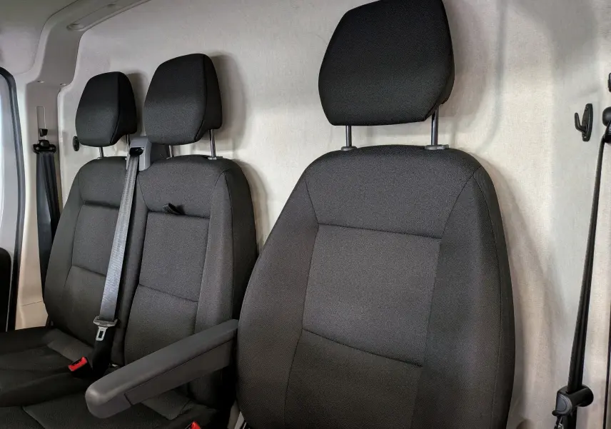 Vue intérieure rapprochée des sièges avant en tissu noir du Fiat Ducato Fourgon blanc, version 2026, avec accoudoir côté droit.