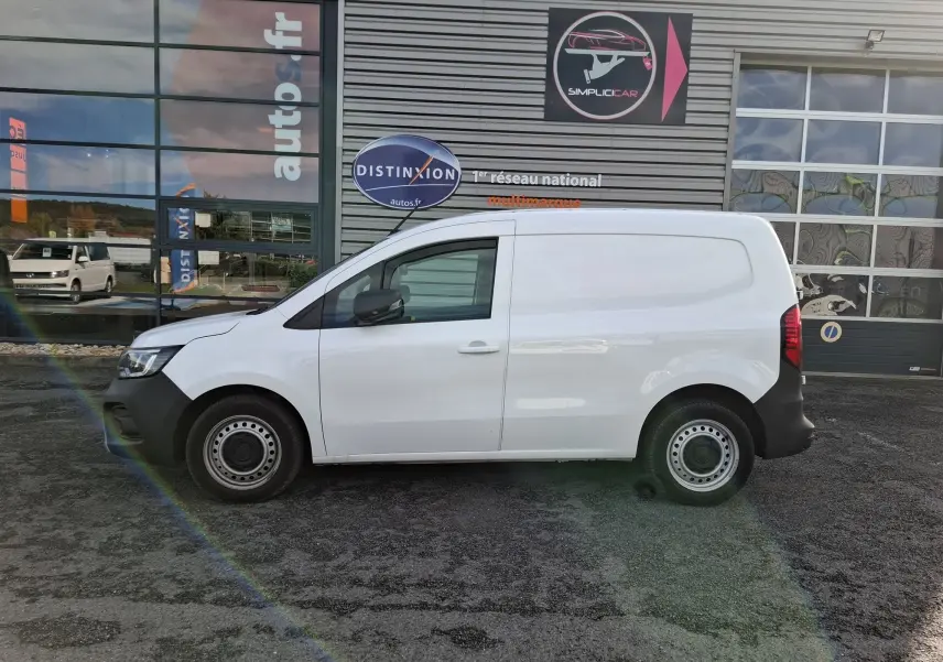 Profil latéral droit d’un Renault Kangoo Pro blanc stationné devant un bâtiment commercial avec jantes acier noires.