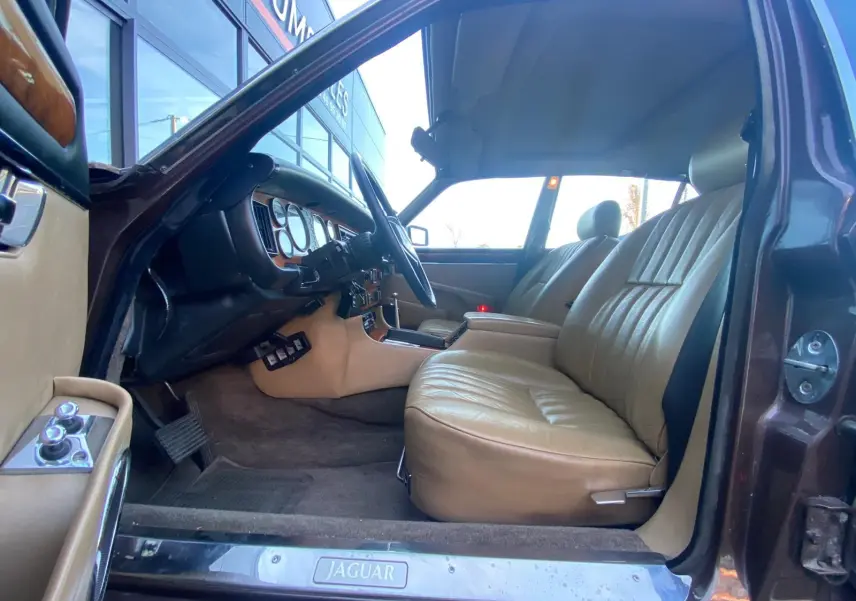 Intérieur beige cuir vu côté conducteur d'une Jaguar XJ6 Série 3 4.2 Sovereign marron de 1985 avec tableau de bord en bois.