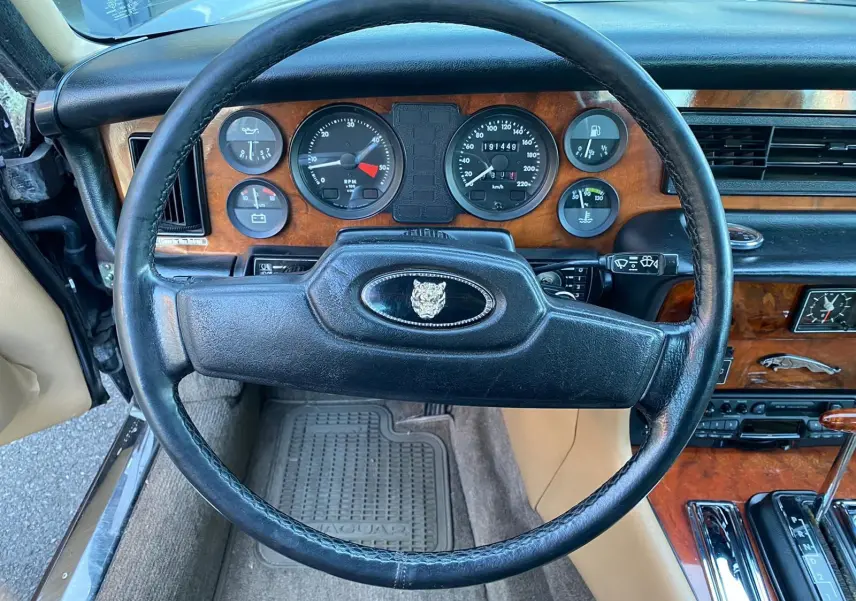 Vue intérieure centrée sur le volant noir et le tableau de bord en bois de la Jaguar XJ6 Série 3 marron de 1985.