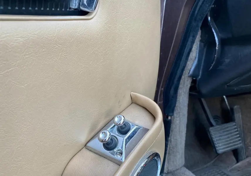 Gros plan sur la portière côté gauche marron d'une Jaguar XJ6 Série 3 4.2 Sovereign de 1985 avec commandes chromées.