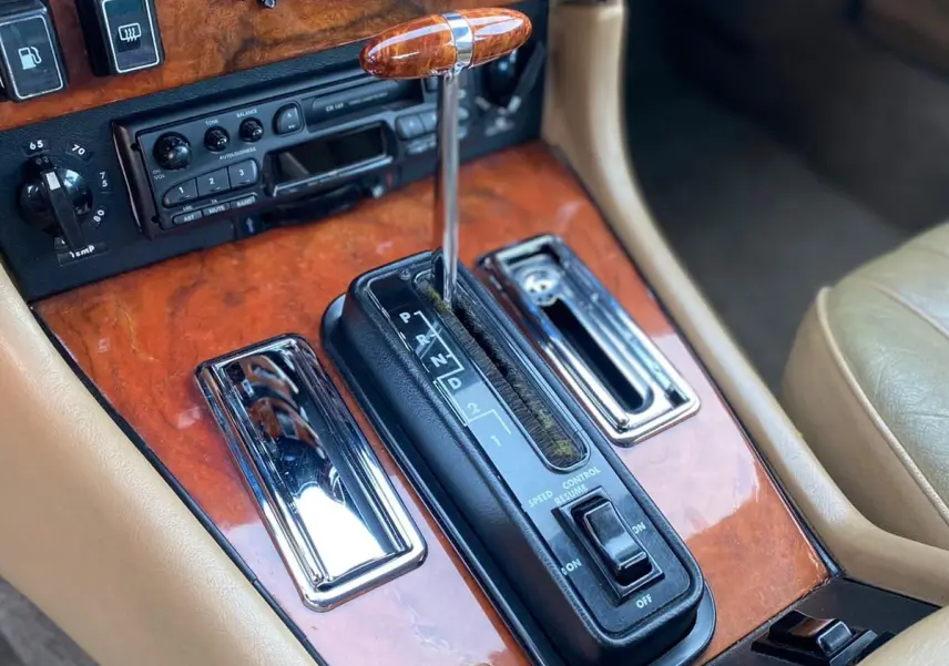 Gros plan sur la console centrale en bois marron de la Jaguar XJ6 Série 3 4.2 Sovereign de 1985 avec levier de vitesses automatique.