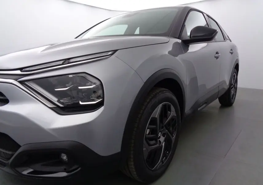 Vue 3/4 avant droit d'une Citroën C4 2023 gris Artense métal avec phares modernes et jantes noires bicolores.