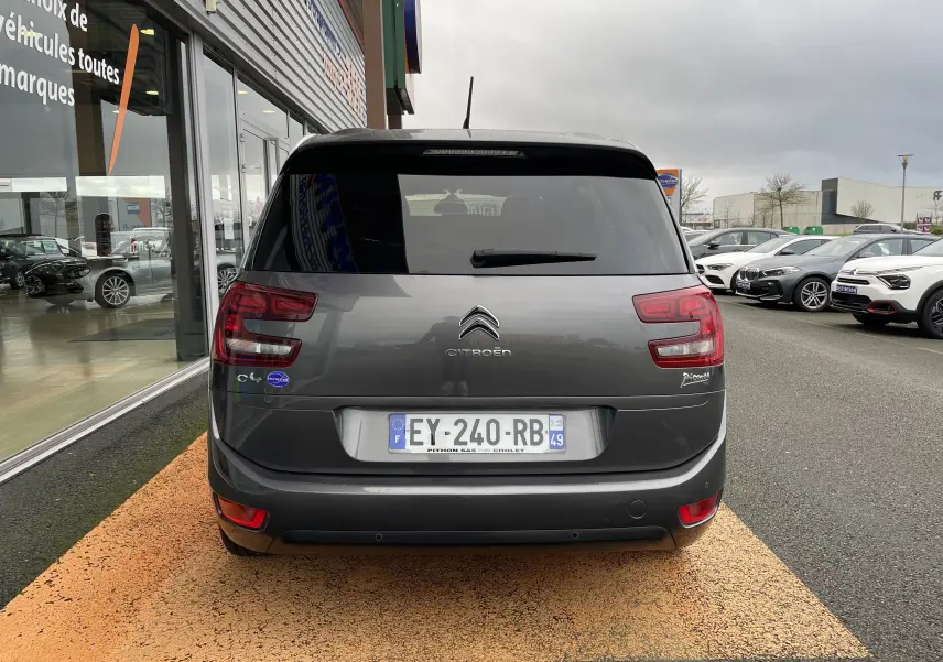 Vue arrière d'un Citroën Grand C4 Picasso gris garé devant un showroom, avec feux arrière distinctifs et vitre teintée.