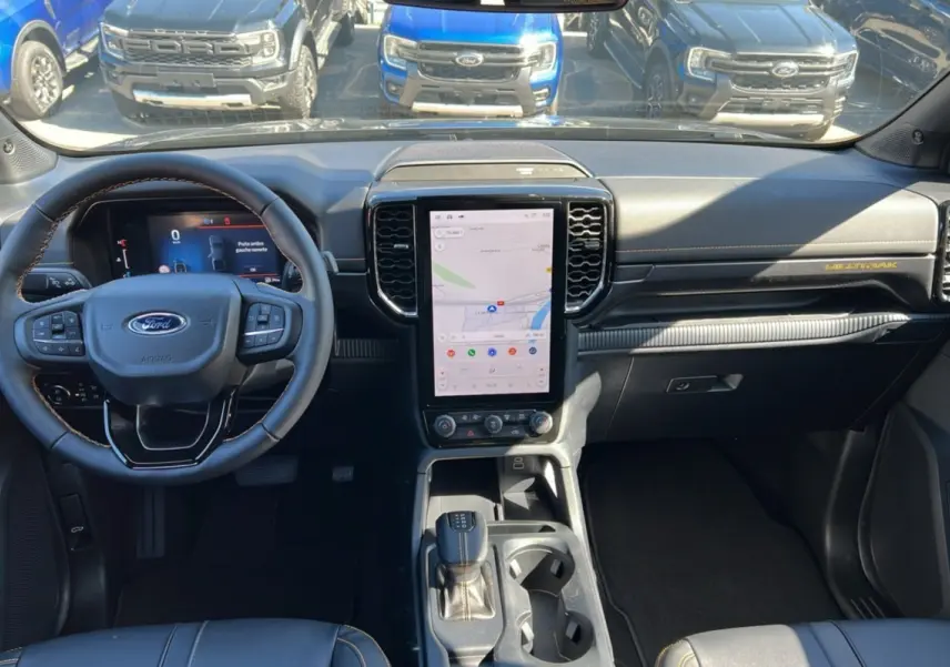 Vue intérieure du Ford Ranger 2025 Wildtrak Plus, tableau de bord noir avec écran tactile vertical et volant multifonction.
