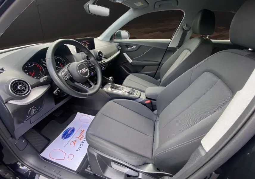 Intérieur avant de l'Audi Q2 35 TFSI 2023 en tissu noir, vue côté conducteur avec tableau de bord et volant visibles.