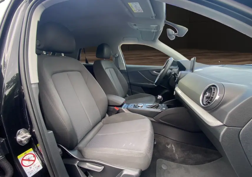 Intérieur avant droit de l'Audi Q2 noir mito 2023, sièges tissu noir et tableau de bord moderne avec écran GPS.
