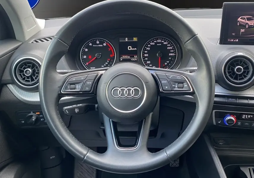 Vue intérieure centrée sur le volant cuir noir de l'Audi Q2 35 TFSI avec tableau de bord et écran GPS visible.